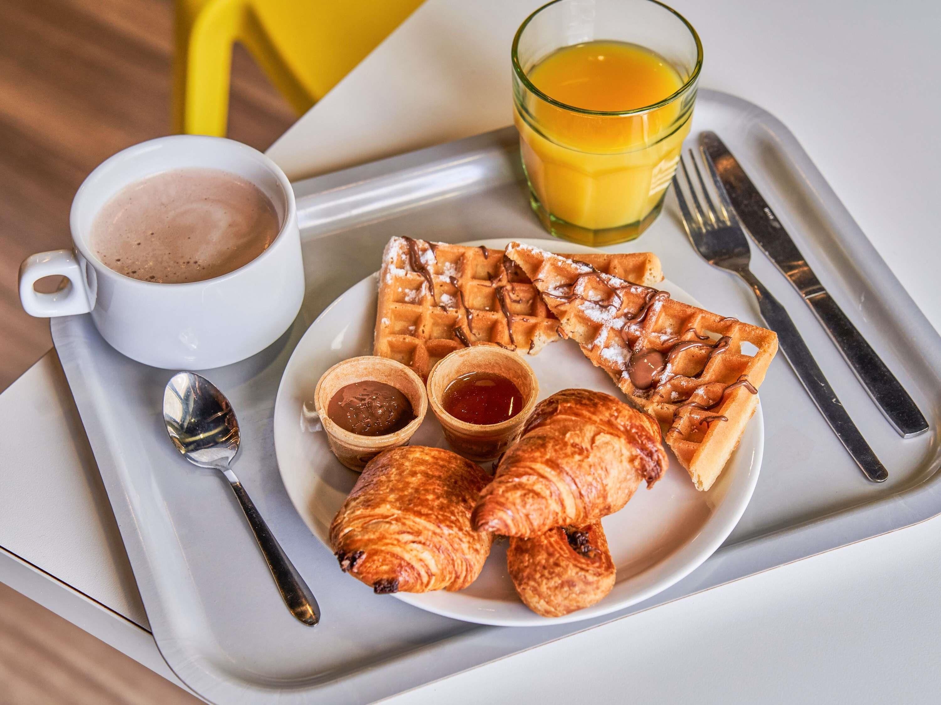 A breakfast tray with waffles, croissants, and a cup of coffee.