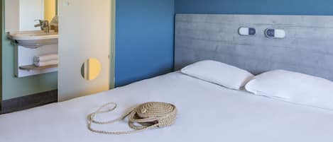 Une chambre d’hôtel avec un lit, une table de chevet, un miroir, une horloge murale et un panneau indiquant « Zzz… ».