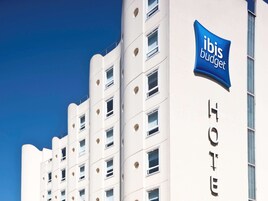 Un bâtiment d’hôtel moderne, avec une enseigne « ibis budget » bien visible et le mot « HÔTEL » écrit sur le côté.