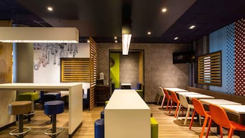 Un interior de restaurante moderno con mesas altas y sillas coloridas, un separador de madera y una pared con diseño.