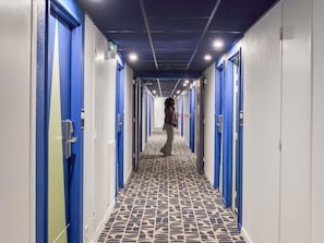 A hotel corridor with blue doors, patterned floor tiles, and overhead lighting. - ibis budget Bordeaux Centre Gare Saint Jean (Bordeaux)