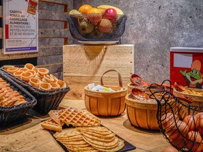 A buffet with various food items including waffles, bread, and a fruit bowl. - ibis budget Bordeaux Centre Gare Saint Jean (Bordeaux)