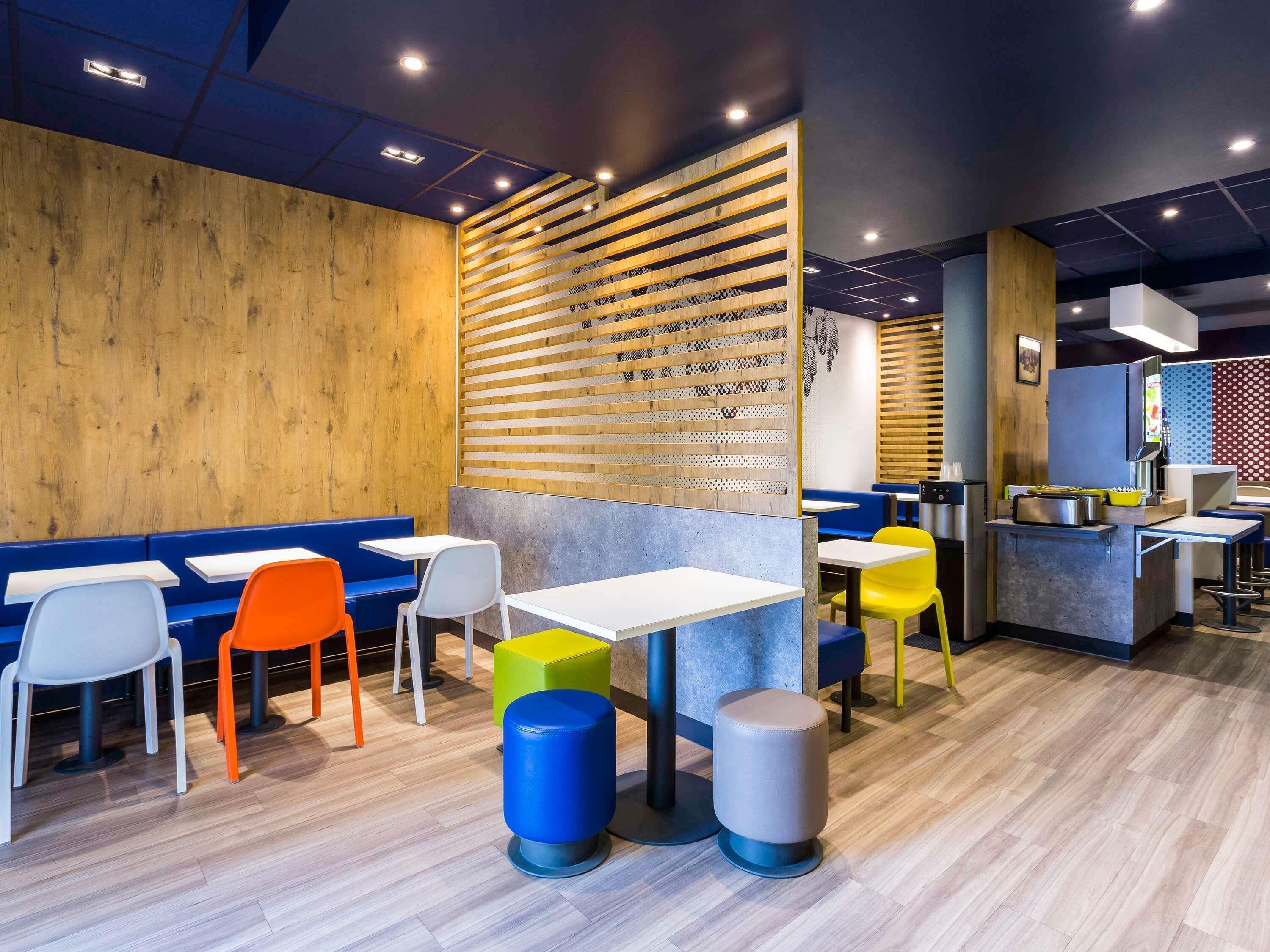 Interior de restaurante con paneles de madera, asientos en tonos azul y naranja, y una barra con máquina de café.