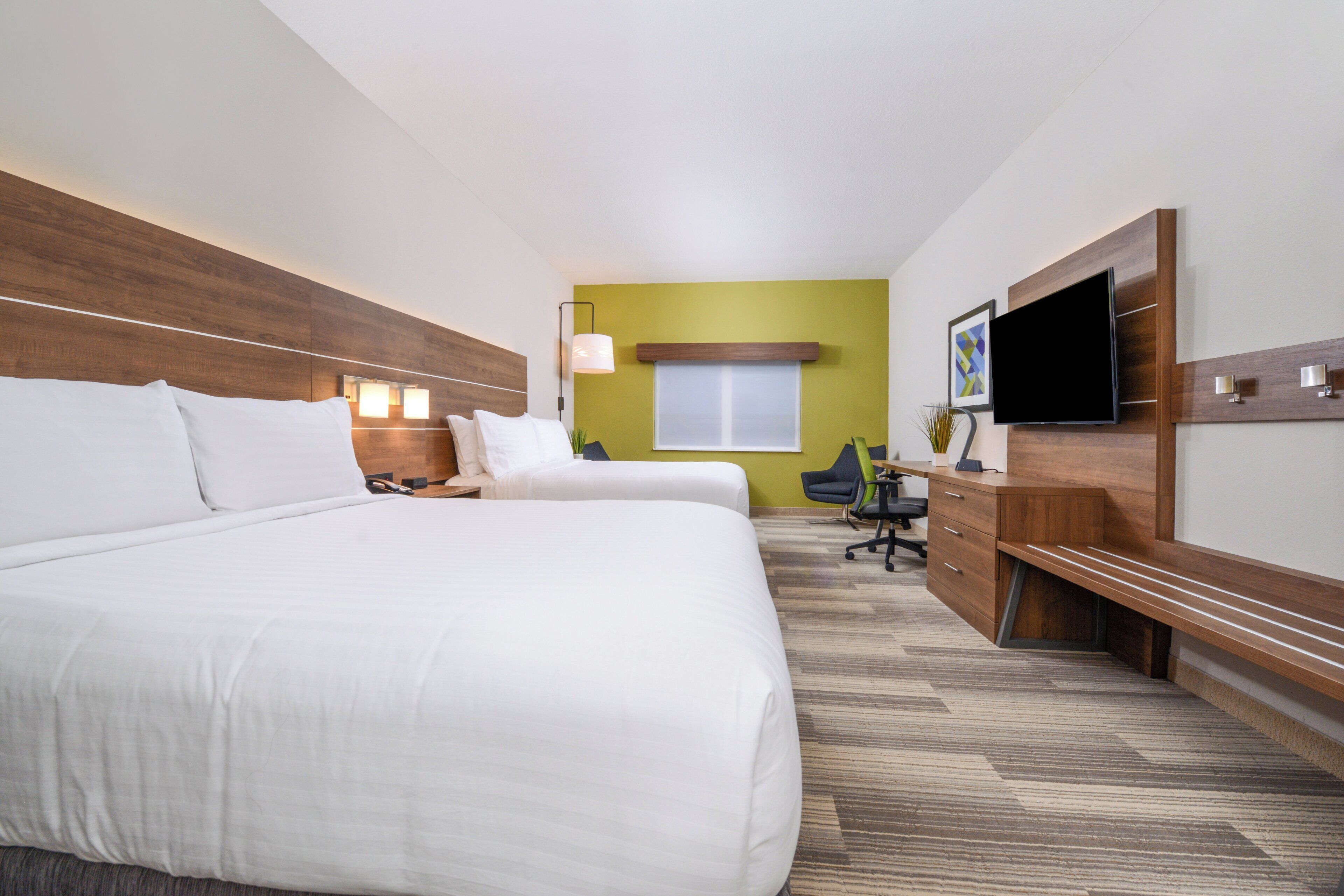 A hotel room with two beds, a desk, a chair, a TV, and a window.