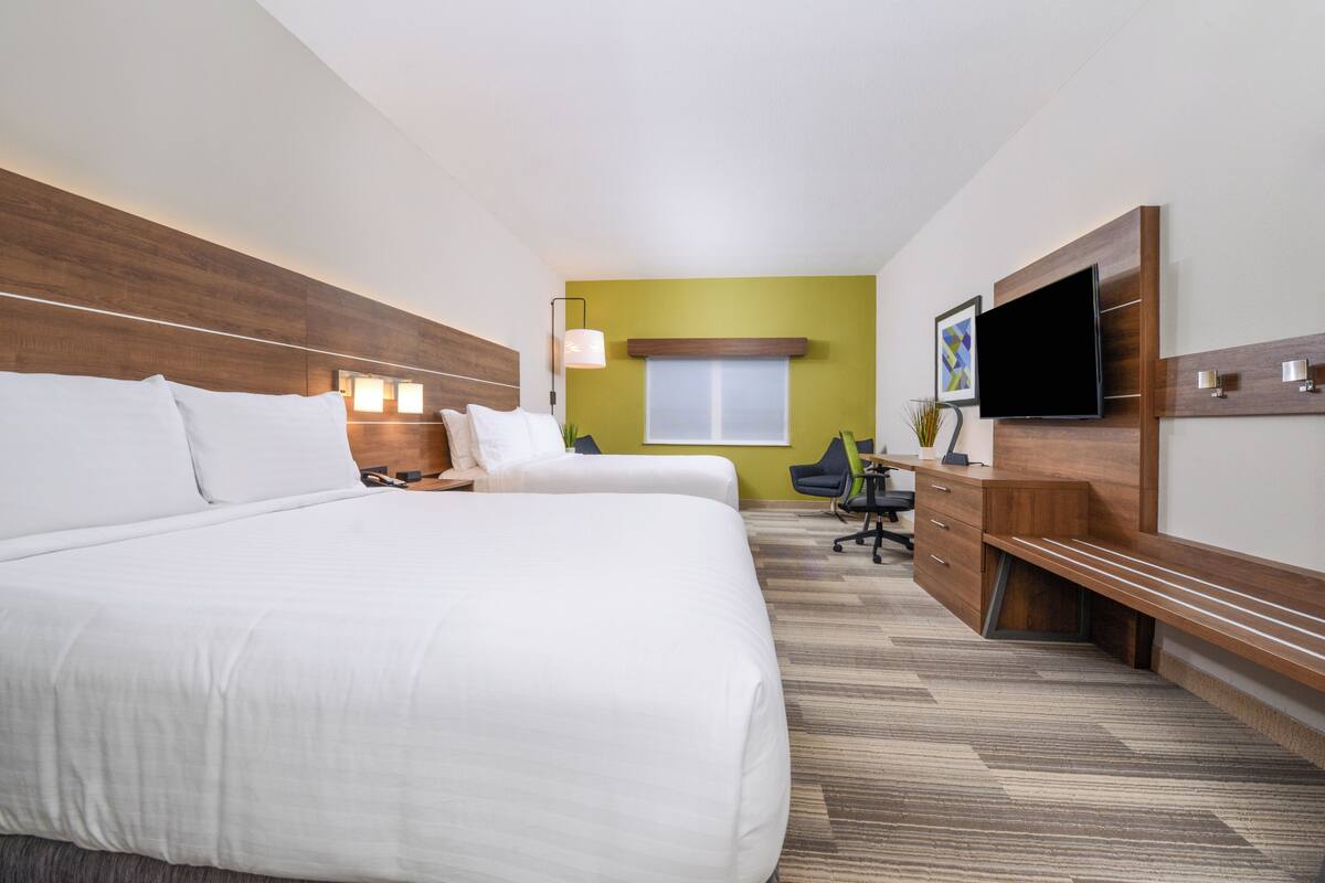 A hotel room with two beds, a desk, a chair, a TV, and a window.
