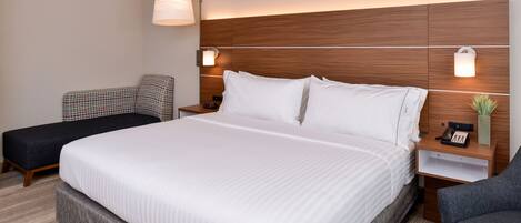 A hotel room with a large bed, a bedside table with a lamp, a chair, and a small table with a phone.