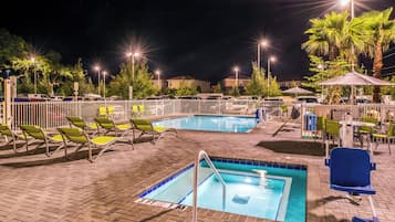 A nighttime swimming pool area with two pools, lounge chairs, and umbrellas.