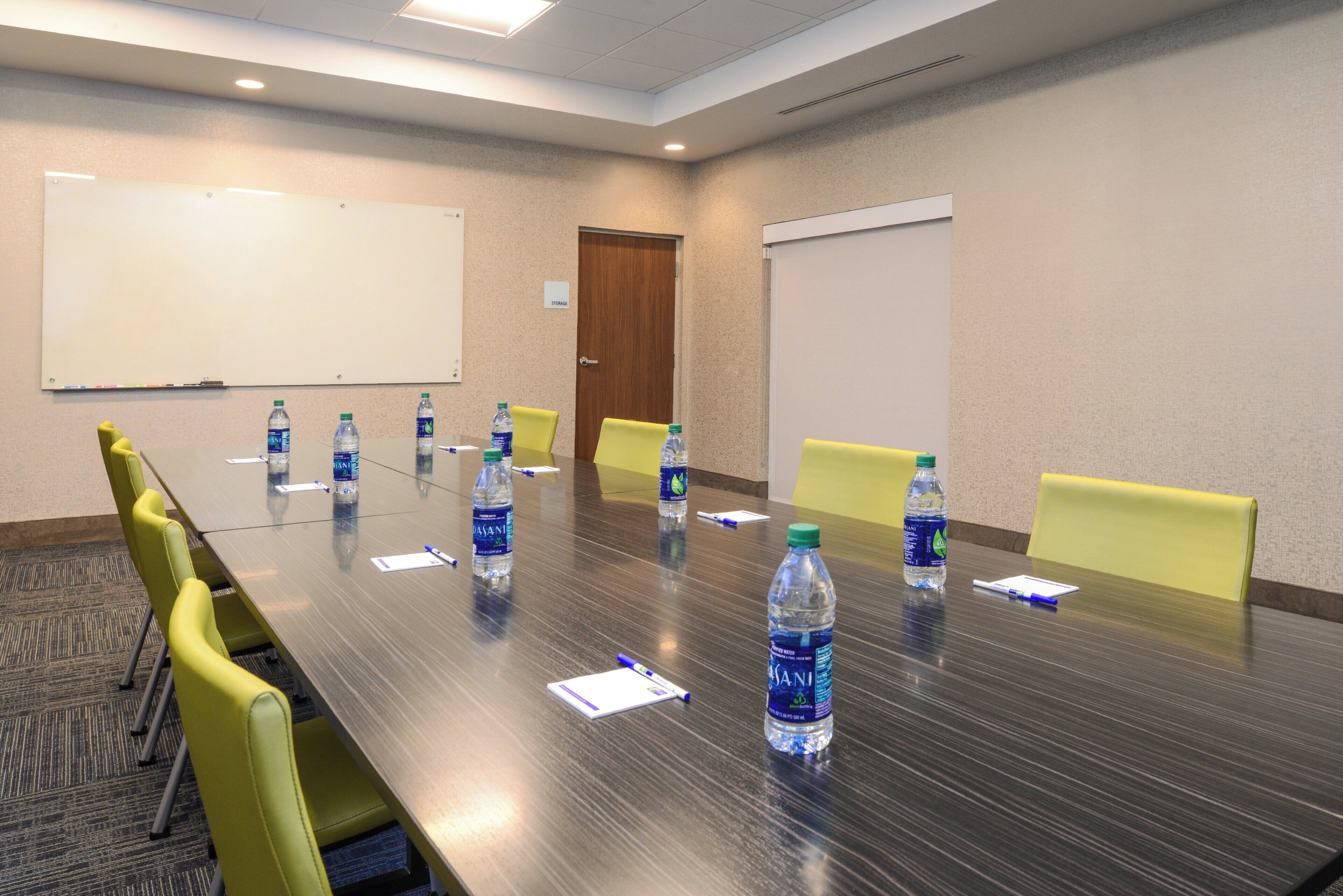 Un salón de conferencias con una larga mesa, sillas amarillas y botellas de agua.
