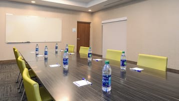 Un salón de conferencias con una larga mesa, sillas amarillas y botellas de agua.