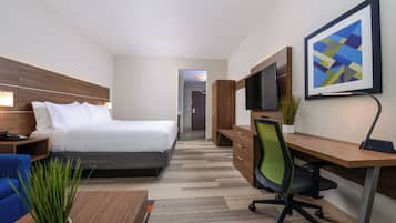 A hotel room with a bed, a desk with a chair, a TV, and a plant.