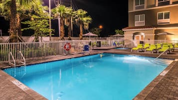 A nighttime swimming pool area with a fence, palm trees, and lounge chairs.