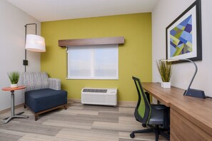 A compact office space with a desk, chair, air conditioner, and a small couch.