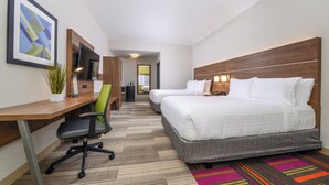 Hotellihuone, jossa on työpöytä, kaksi sänkyä, televisio ja värikäs matto.