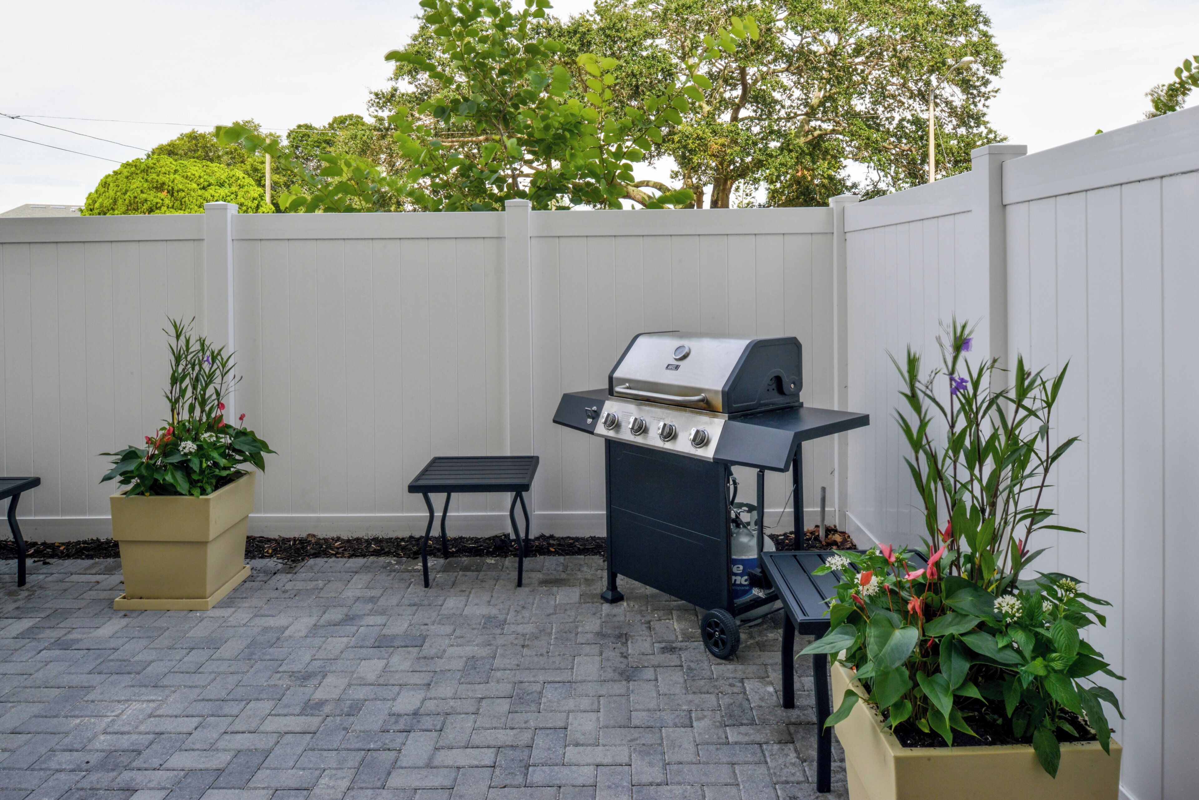 Une terrasse extérieure équipée d’un barbecue, d’une table et de plantes en pot.