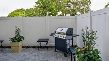 Une terrasse extérieure équipée d’un barbecue, d’une table et de plantes en pot.
