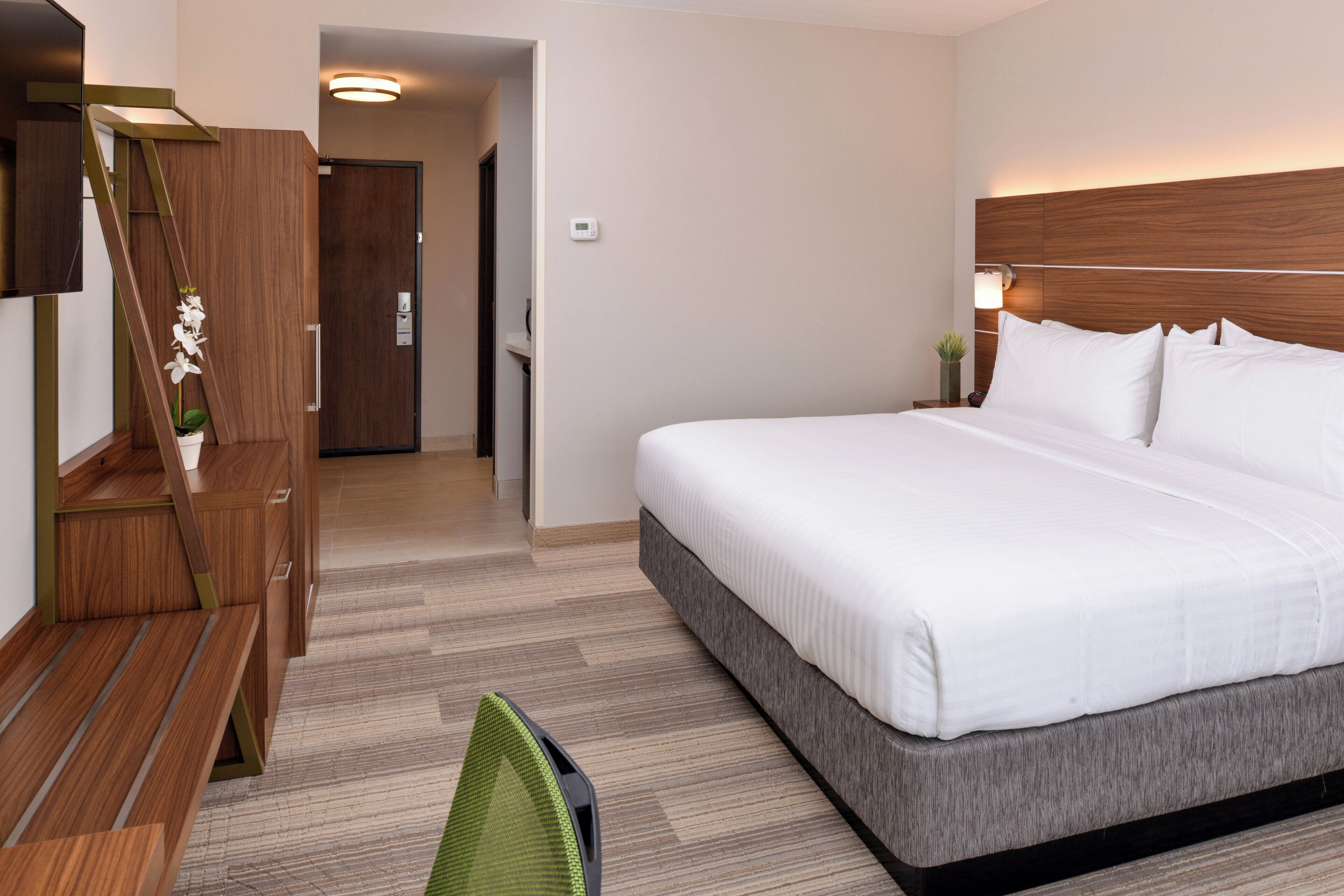 Una habitación de hotel con cama, escritorio, silla, televisor y puerta.