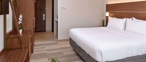 Una habitación de hotel con cama, escritorio, silla, televisor y puerta.