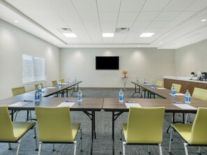 Un salón de conferencias con una larga mesa, sillas, una pantalla de televisión y una zona de kitchenette.