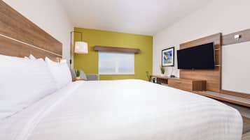 Une chambre d’hôtel avec un grand lit, un téléviseur à écran plat fixé au mur, une fenêtre donnant sur un beau paysage et une petite table avec une lampe.