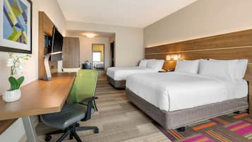 Ein Hotelzimmer mit Schreibtisch, zwei Betten, Fernseher und einer Zimmerpflanze.