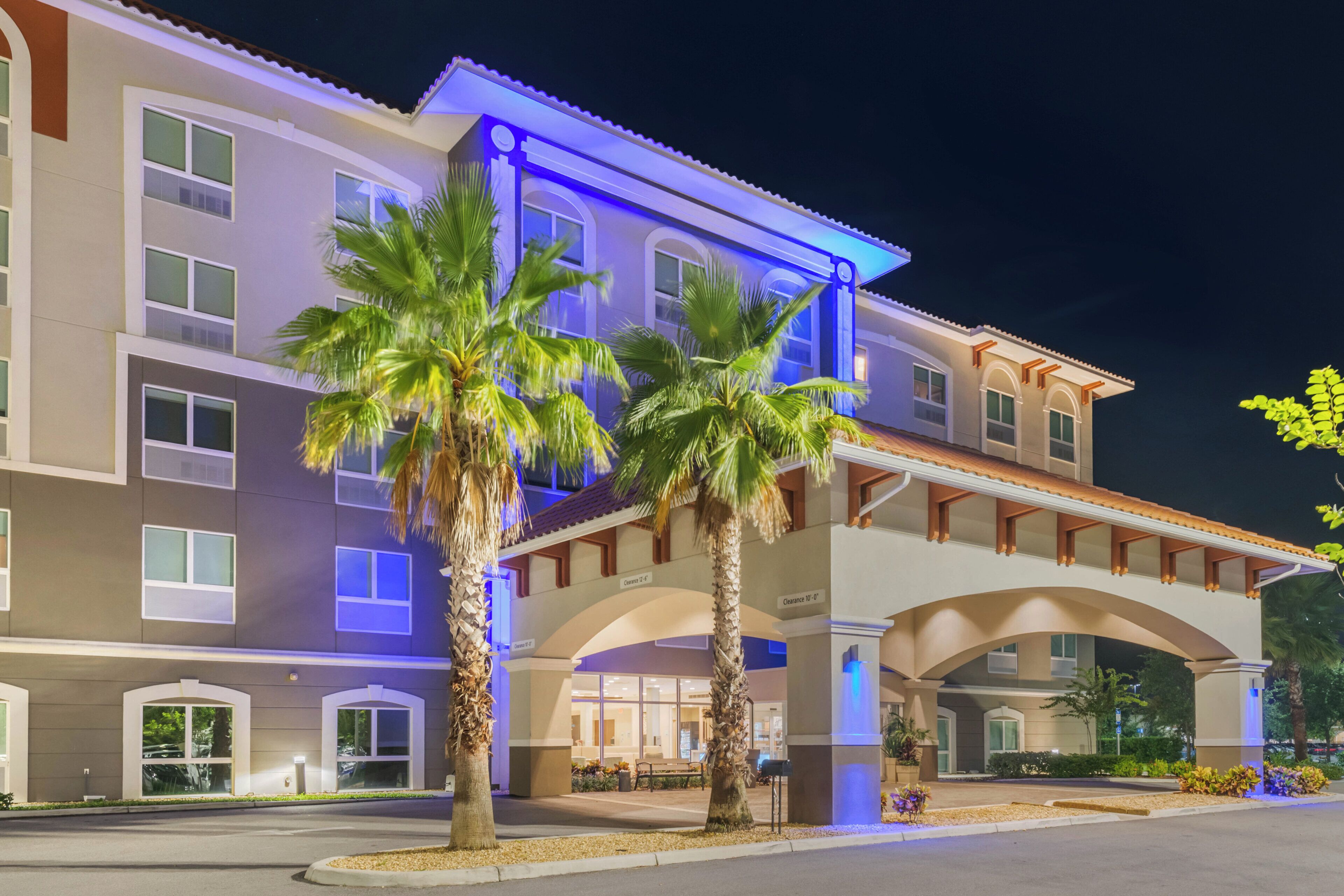 A hotel with multiple floors, a covered entrance, and palm trees in the foreground.