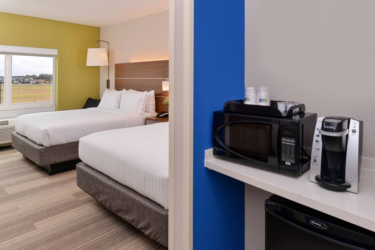 A hotel room with two beds, a microwave, a coffee maker, and a view of the outside.
