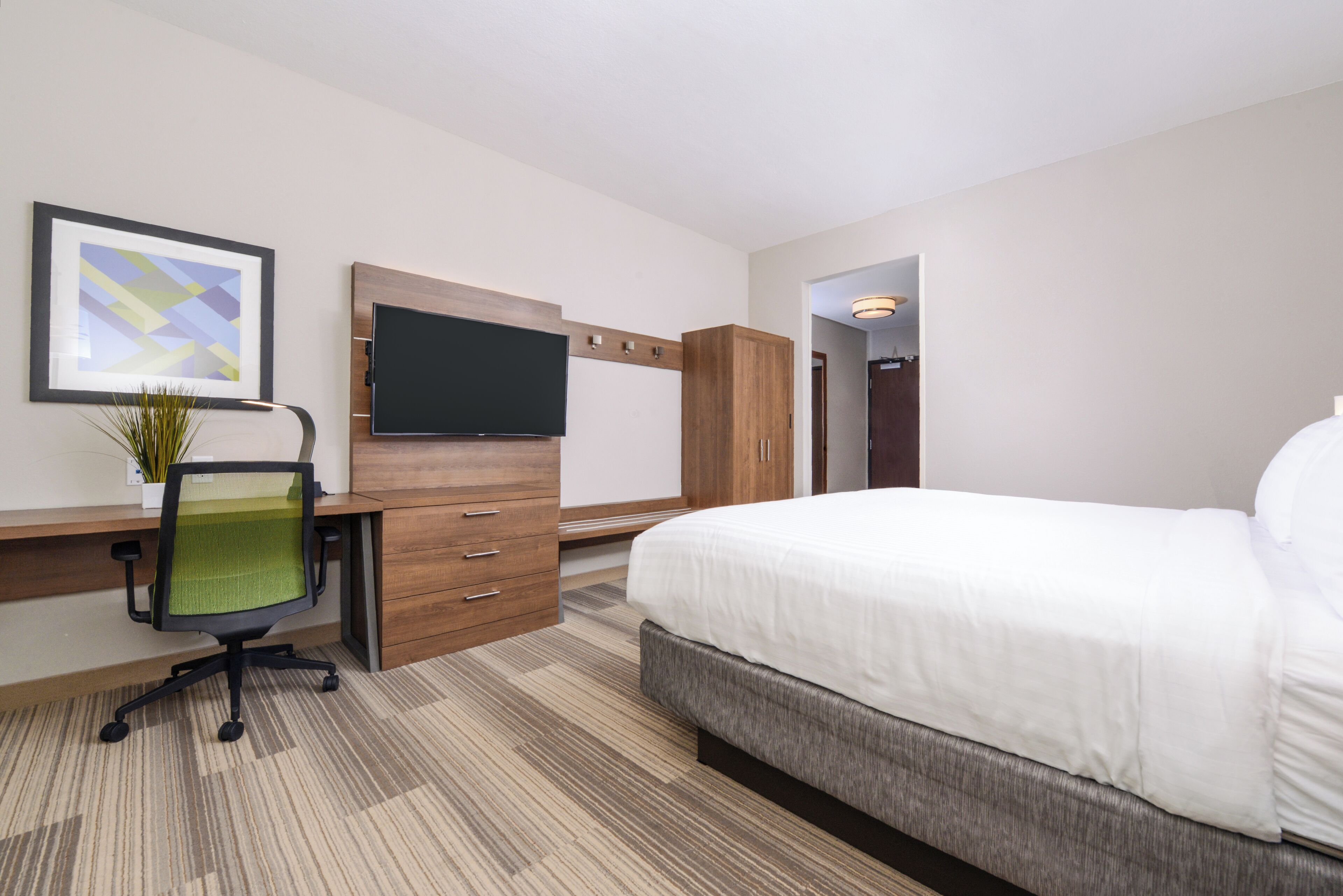 Una habitación de hotel con una cama, un escritorio con silla, televisión y un cuadro en la pared.