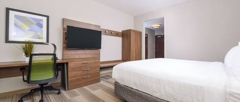 Una habitación de hotel con una cama, un escritorio con silla, televisión y un cuadro en la pared.
