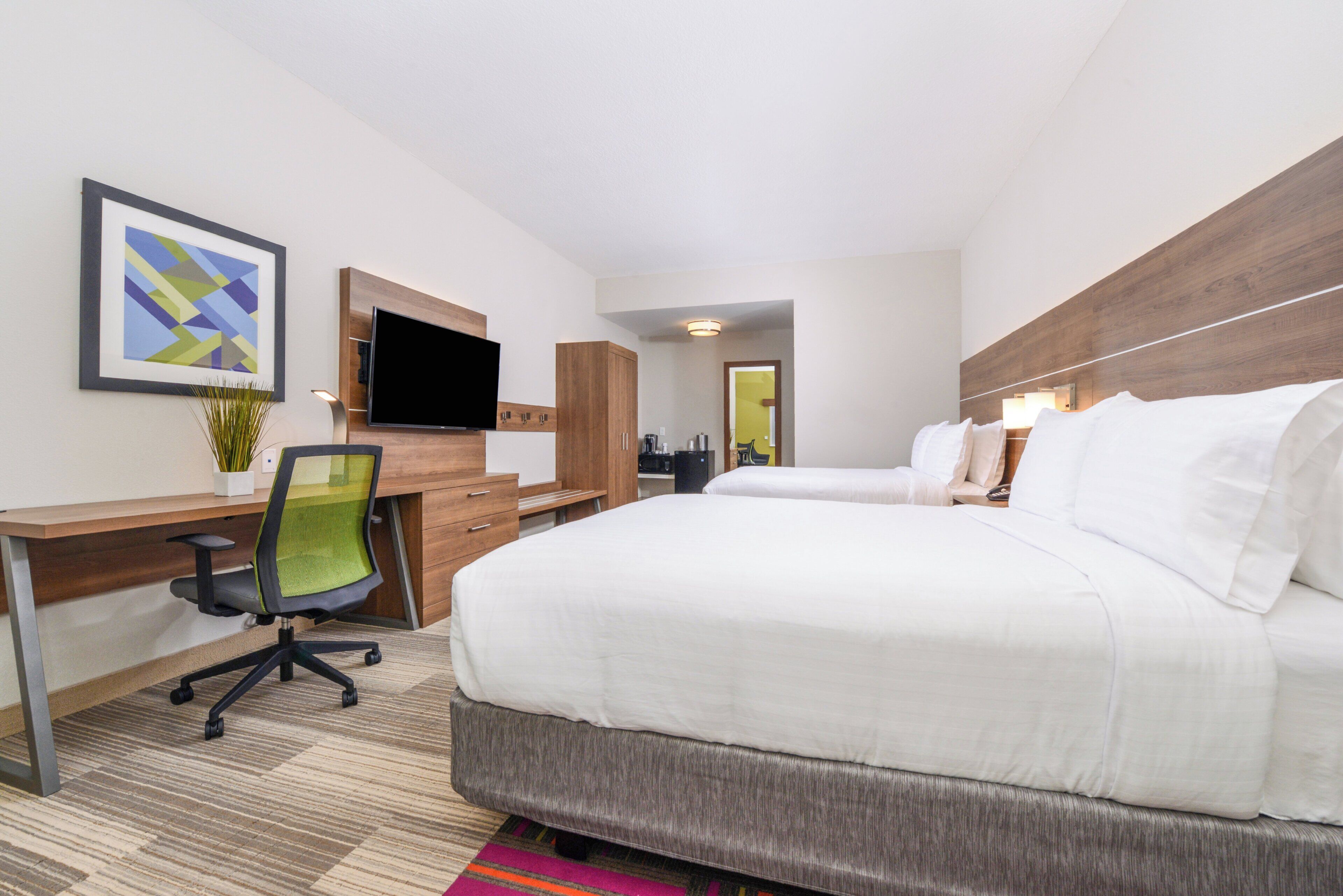 A hotel room with a bed, desk, chair, television, and artwork.