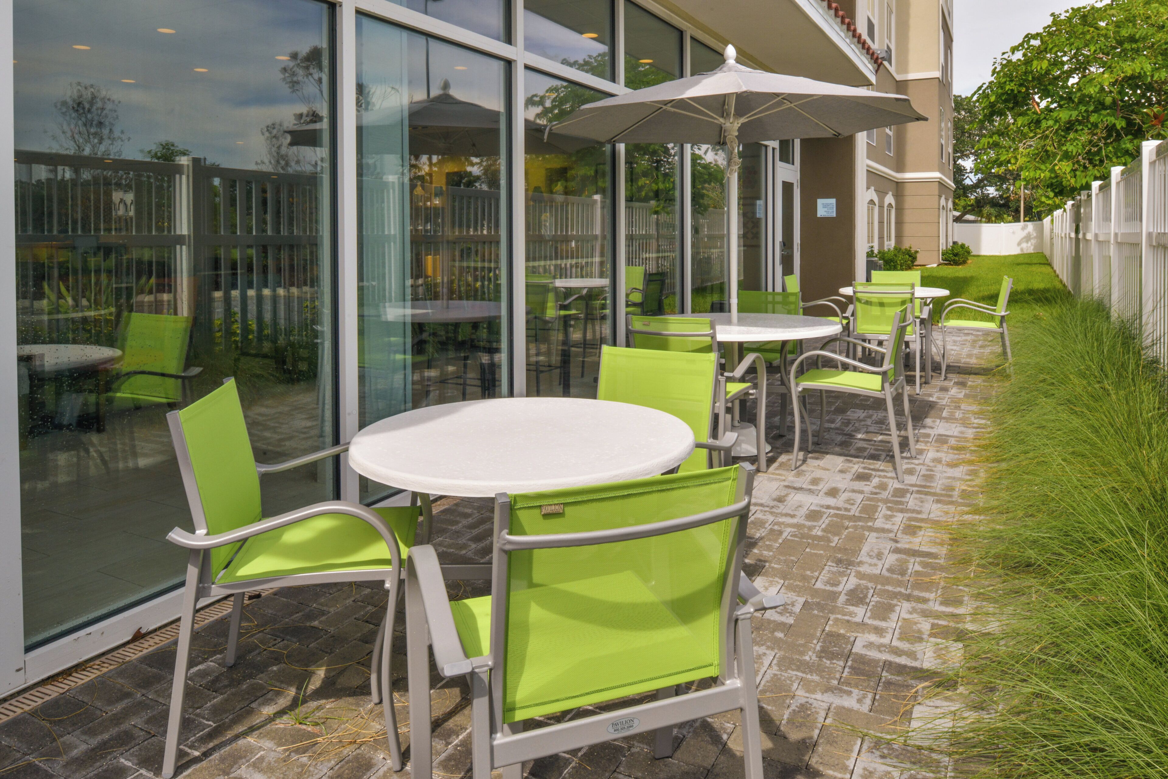 An outdoor seating area with tables and chairs, a glass wall, and a white umbrella.