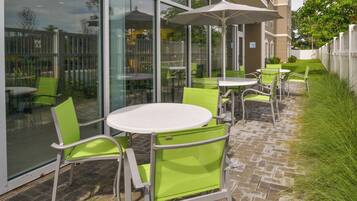 An outdoor seating area with tables and chairs, a glass wall, and a white umbrella.