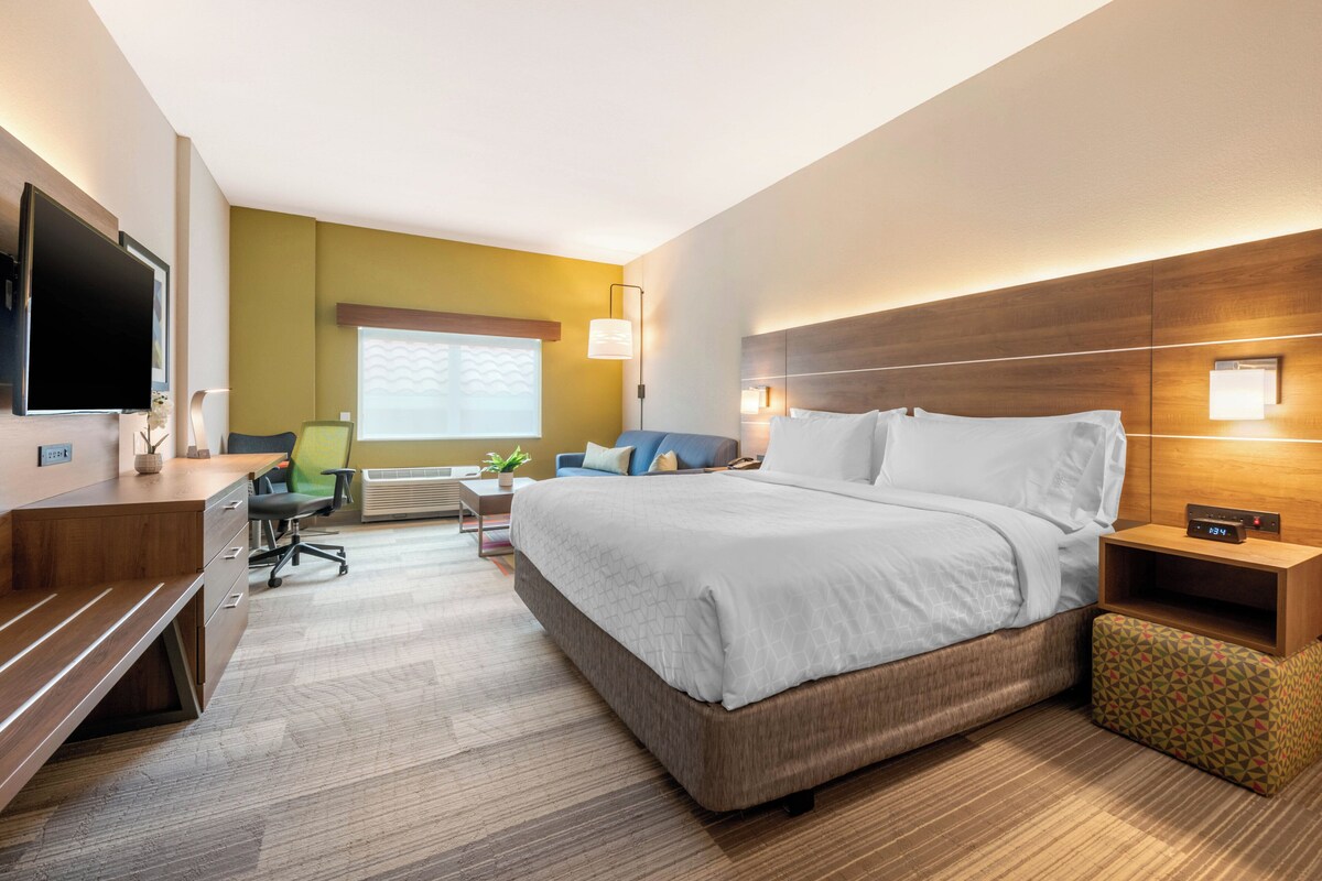 Habitación de hotel con cama, escritorio, silla, televisor y ventana con persianas.