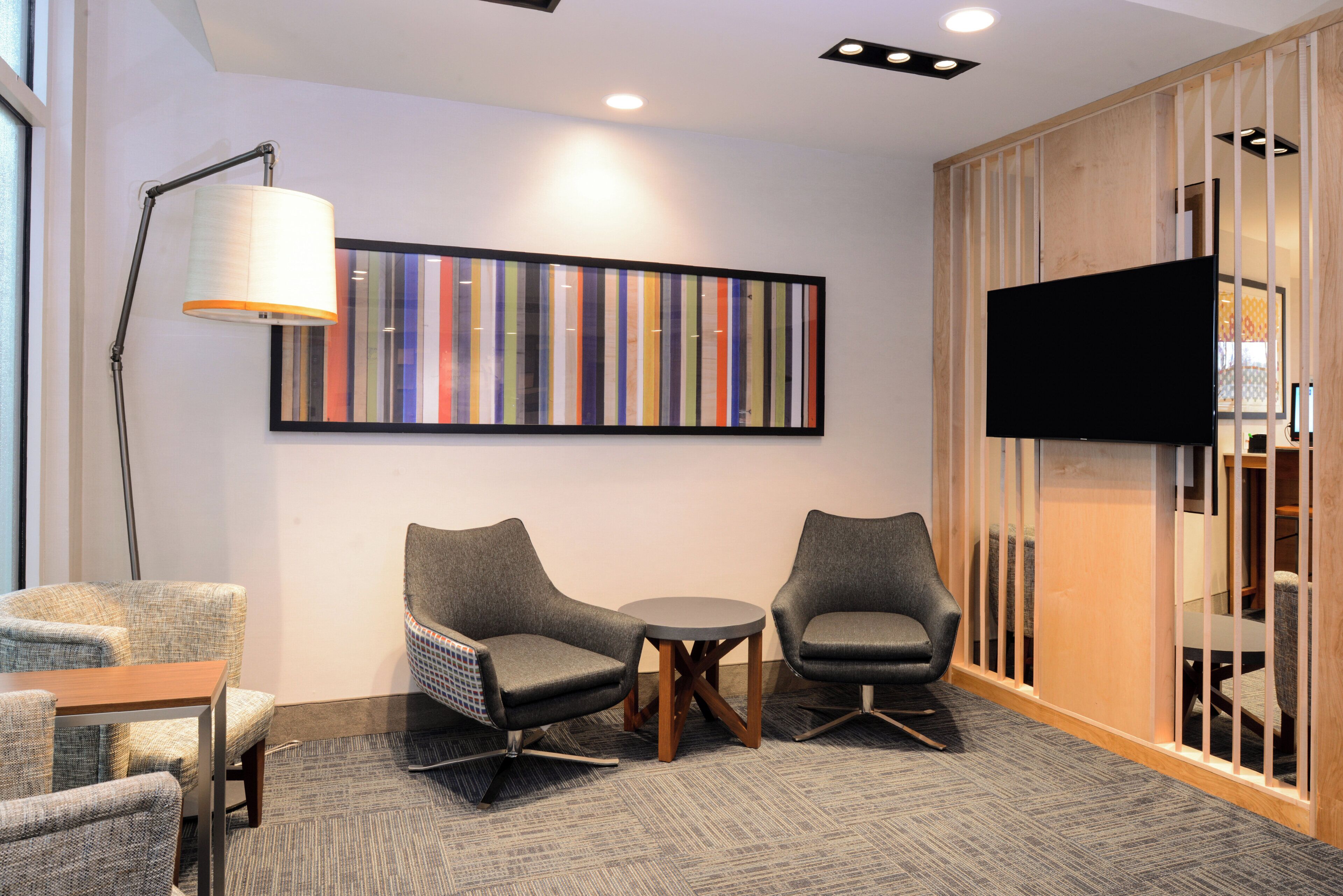A modern room with two grey armchairs, a small round table, a floor lamp, and a large abstract painting on the wall.
