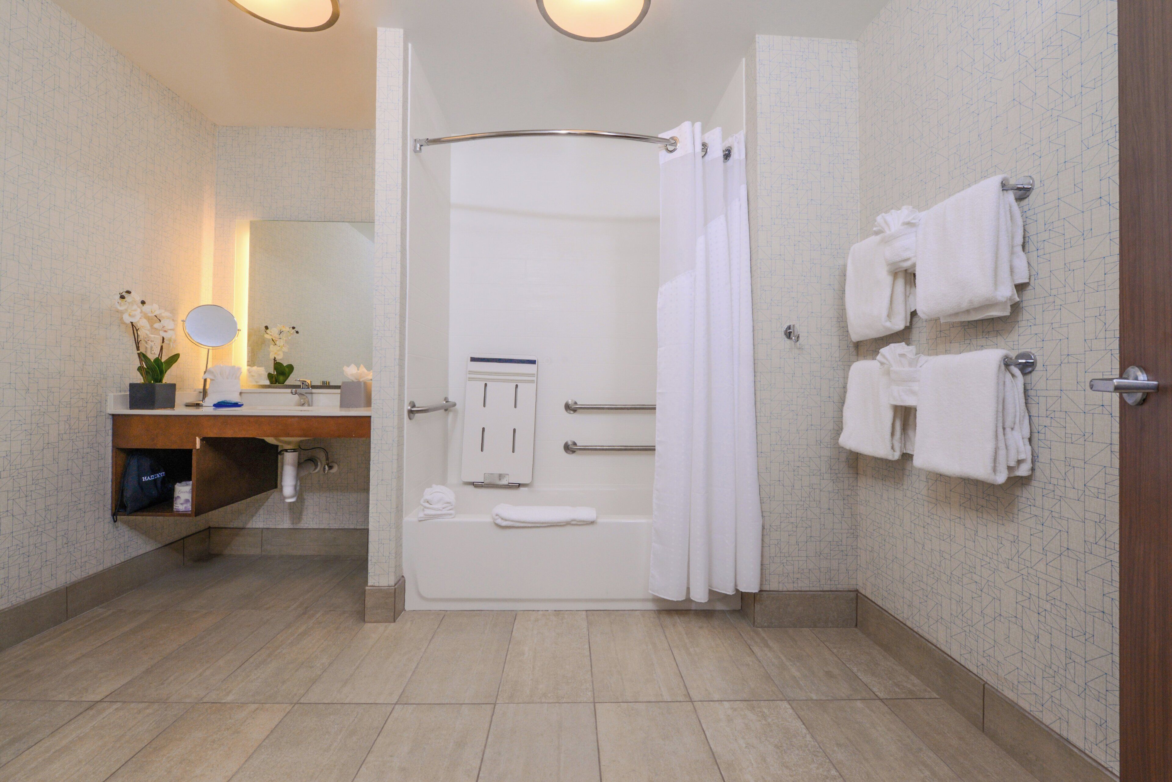 Un baño moderno con bañera, ducha, inodoro, lavamanos y espejo. Hay toallas colgadas en la pared y una planta en maceta sobre el mostrador.
