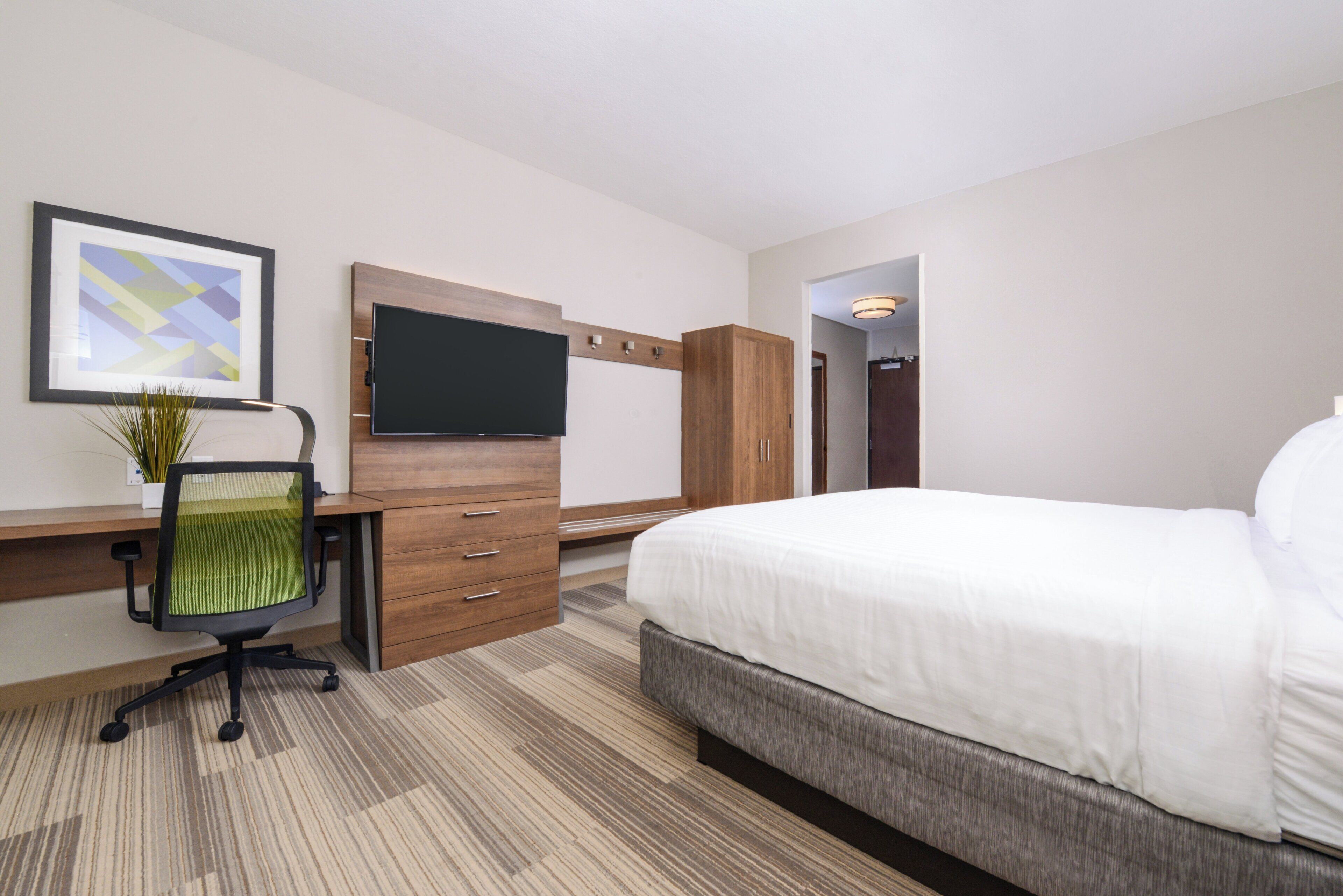 Une chambre d’hôtel avec un lit, un bureau et une chaise, une télévision et un tableau encadré au mur.