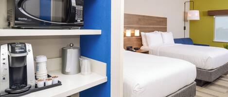 A hotel room with a microwave, coffee maker, and a bed with two pillows.