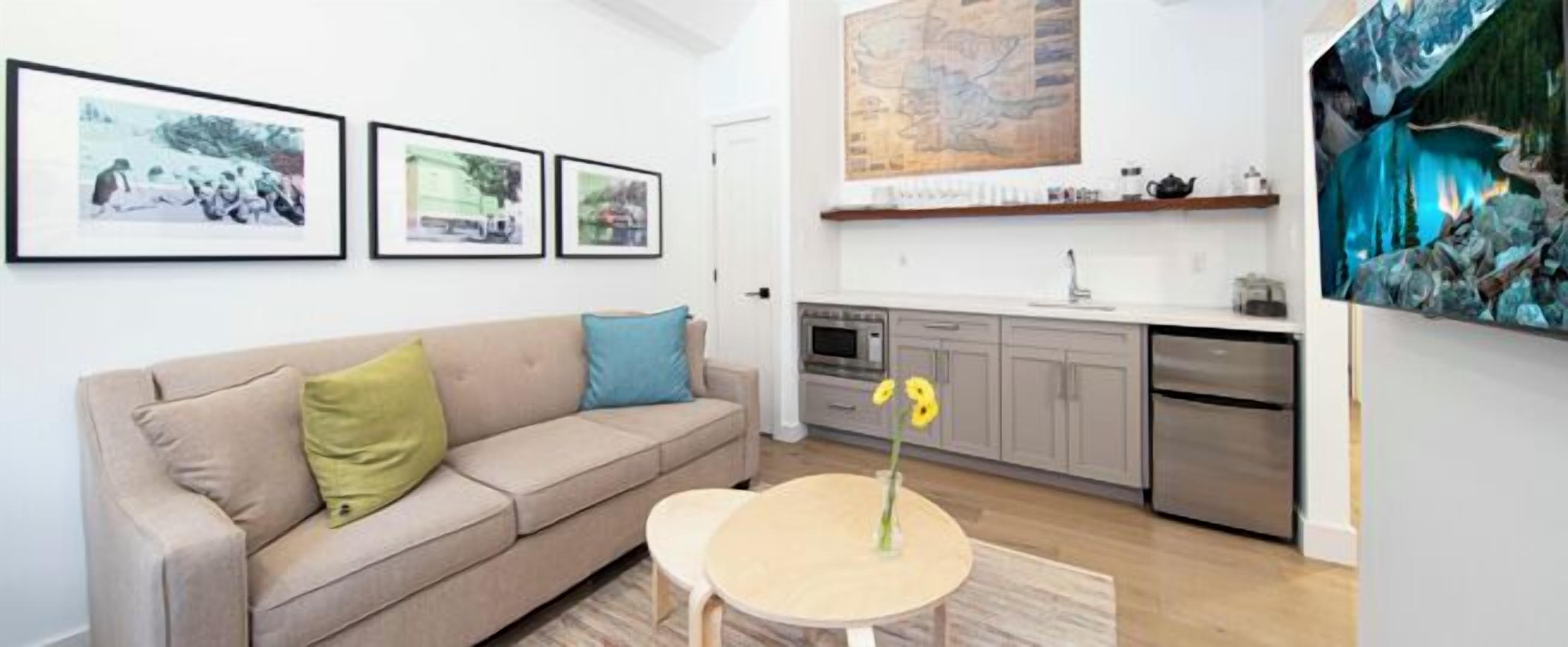 A living room with a sofa, a small round table with a vase, and a kitchen area with cabinets and appliances.