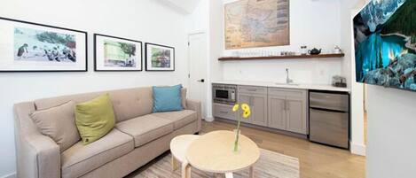 A living room with a sofa, a small round table with a vase, and a kitchen area with cabinets and appliances.