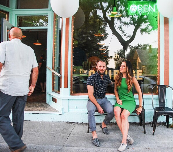 Una pareja sentada frente a un edificio con un cartel que dice 'OPEN'.