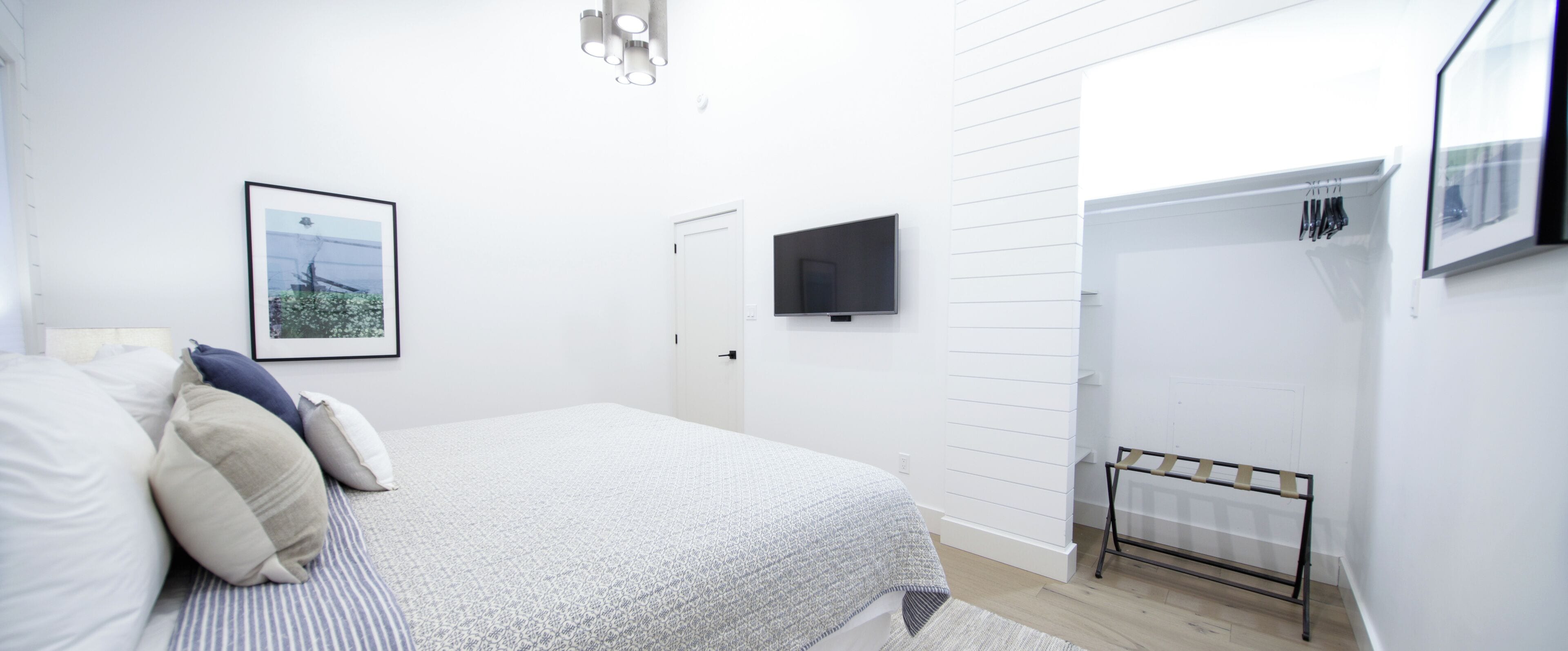 Un dormitorio con cama, televisor, puerta y un perchero con objetos.