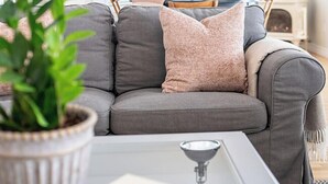 Ein modernes Wohnzimmer mit einem grauen Sofa, einer Topfpflanze und einem weißen Couchtisch.