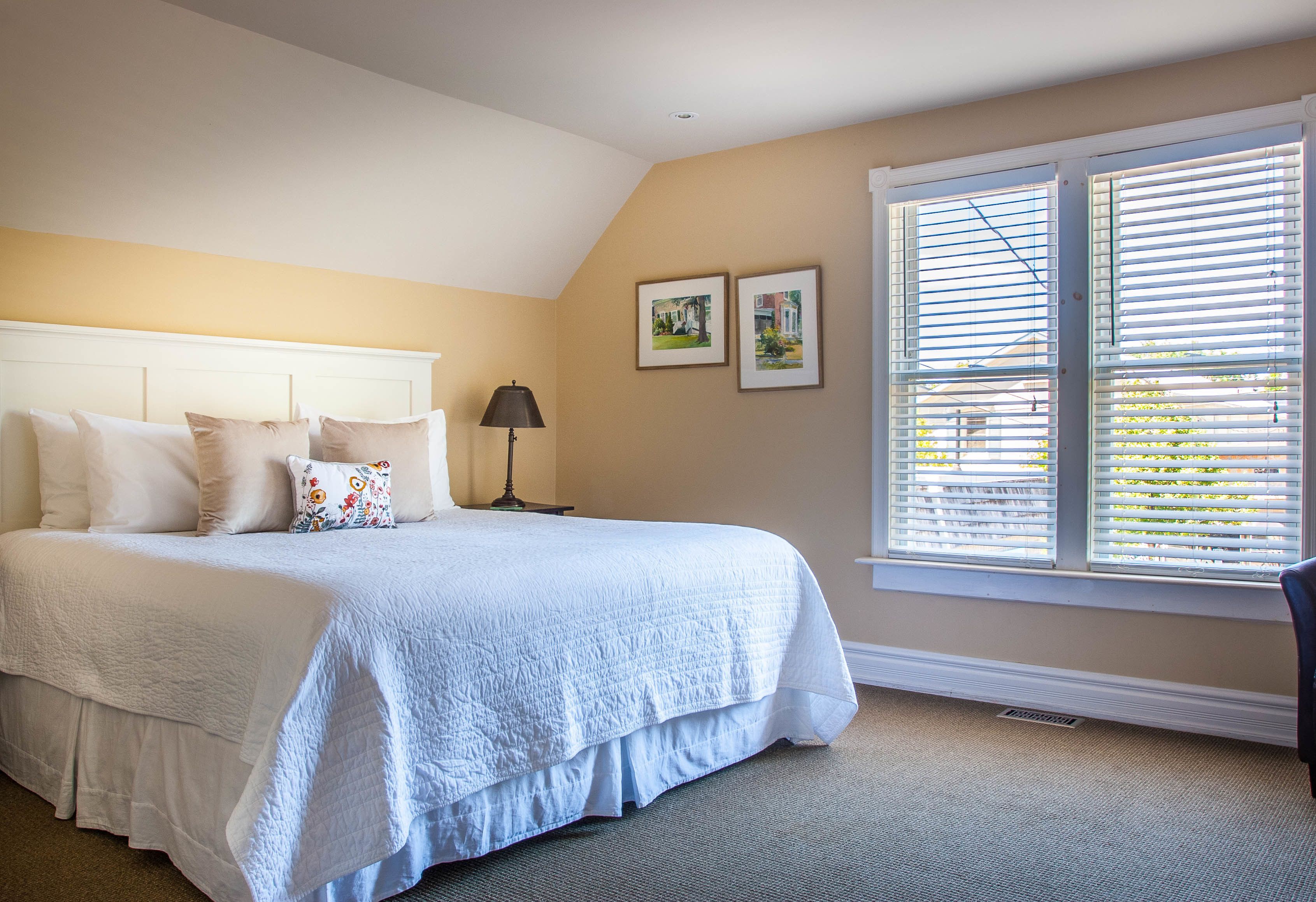 A bedroom with a large bed, a nightstand, a lamp, and two framed pictures on the wall.