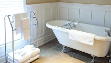 A bathroom with a freestanding bathtub, a towel rack, and a window with blinds.