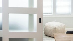 Ein Zimmer mit einer Tür aus Frostglas, einem Fenster mit Jalousien, einem weißen Sitzsack und einem Holztisch.