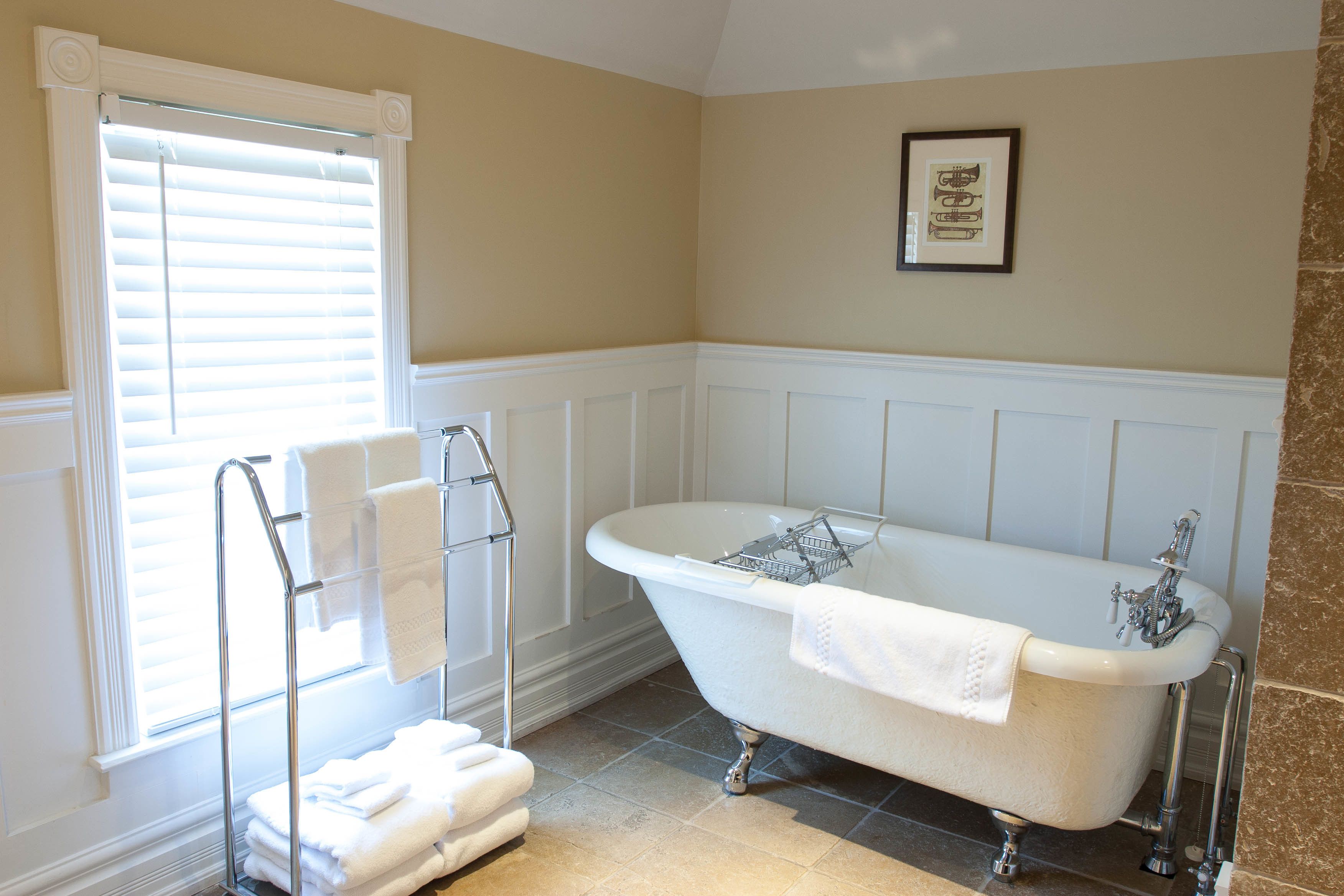 A bathroom with a freestanding bathtub, a towel rack with folded towels, and a framed picture on the wall.