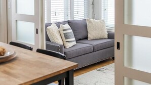 Ein modernes Interieur mit einer Schiebetür zu einem Wohnbereich mit grauem Sofa, Holztisch und Stehlampe.