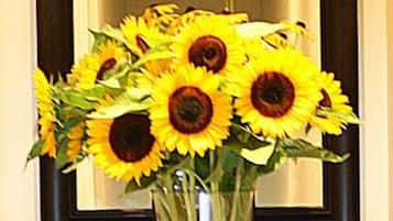 Un aparador de madera con un jarrón de girasoles frente a un espejo.