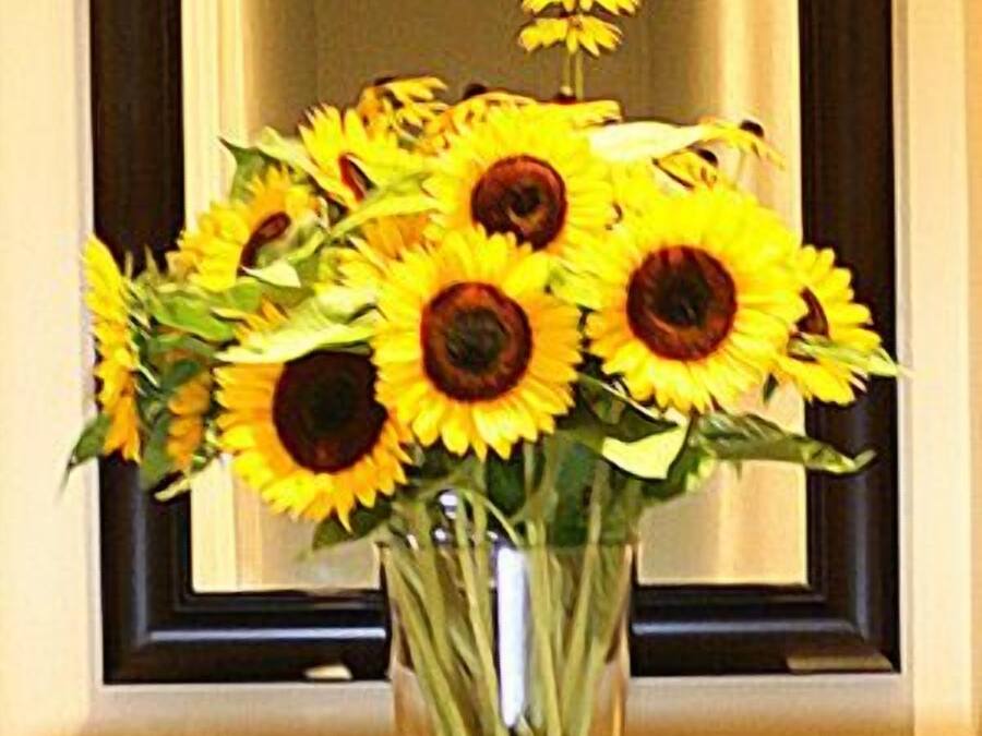 Un aparador de madera con un jarrón de girasoles frente a un espejo.