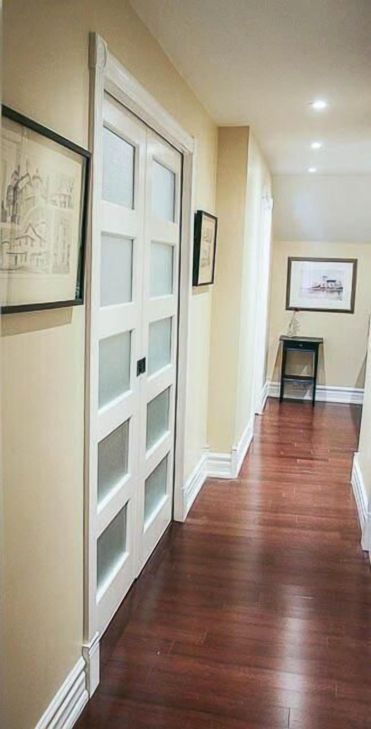 A hallway with wooden flooring, white-framed doors, and framed pictures on the walls.