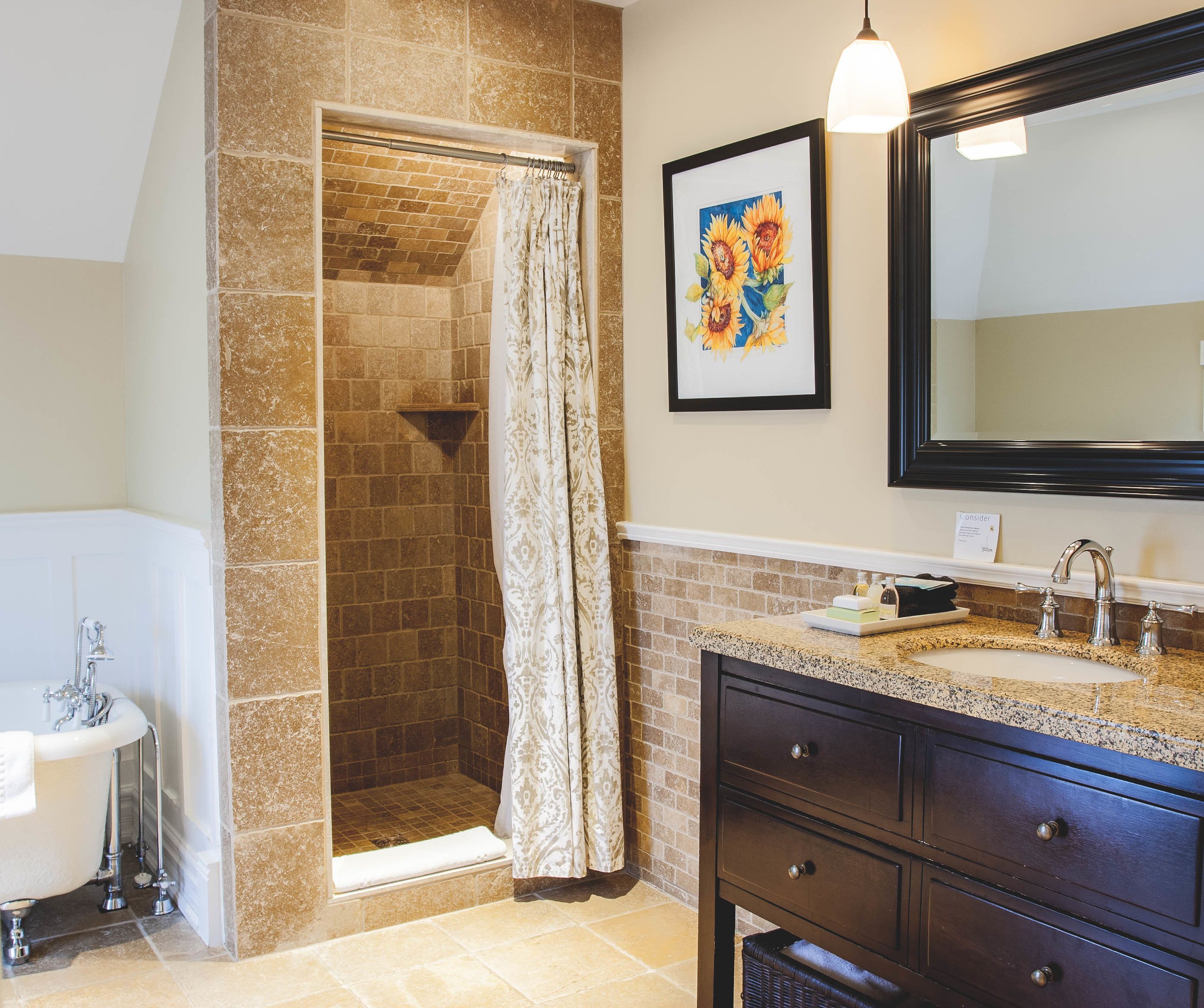 A bathroom with a shower, a sink, a mirror, and a framed picture on the wall.